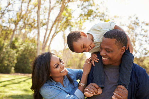 Familia feliz practicando crianza consciente y disciplina positiva - padre cargando a su hijo en los hombros mientras la madre sonríe, demostrando conexión familiar, crianza respetuosa y técnicas de educación positiva
